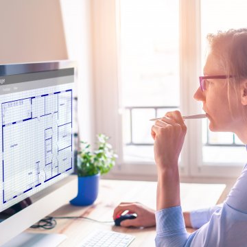 woman looking at computer screen with blueprints 